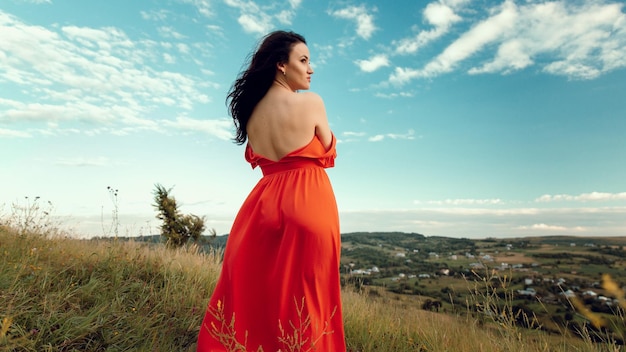 Una mujer con un vestido rojo se para en un campo y mira al cielo.