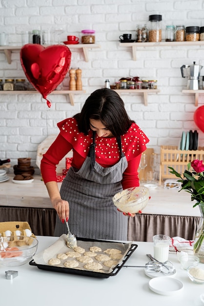 Mujer en vestido rojo y delantal gris haciendo galletas de San Valentín en la cocina
