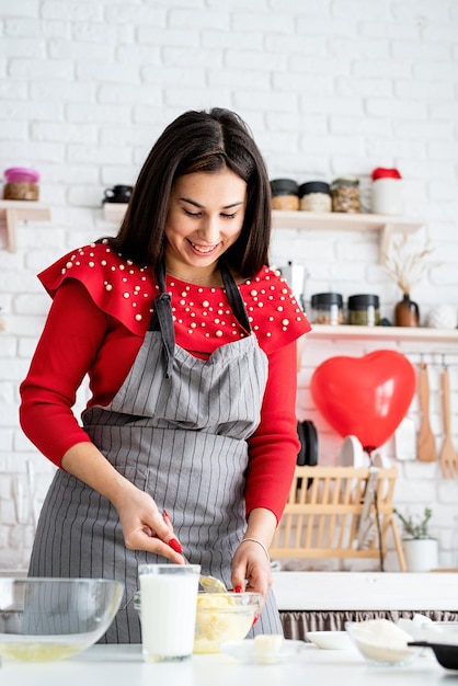 Mujer en vestido rojo y delantal gris haciendo galletas de San Valentín en la cocina