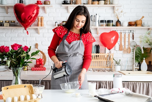 Mujer en vestido rojo y delantal gris haciendo galletas de San Valentín en la cocina