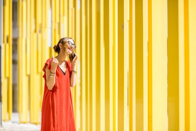 Mujer en vestido rojo hablando con el teléfono en el fondo de la pared del edificio amarillo moderno