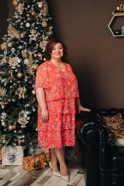 Una mujer con un vestido rojo de pie junto a un árbol de Navidad en un interior decorado para celebrar la Navidad y el Año Nuevo