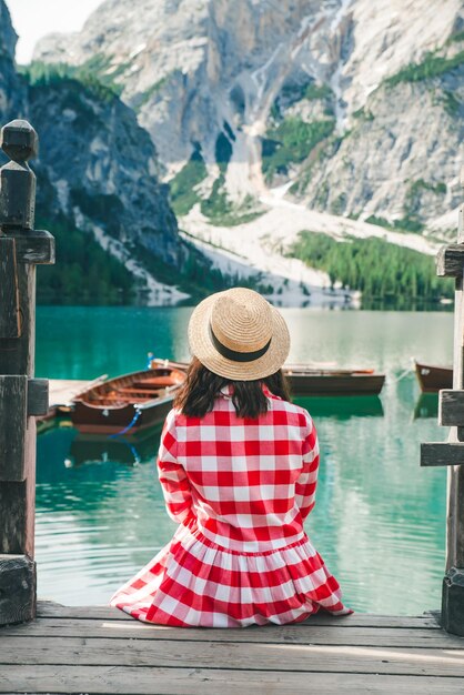 Mujer con vestido rojo sentada en escaleras de madera mirando el lago en las montañas