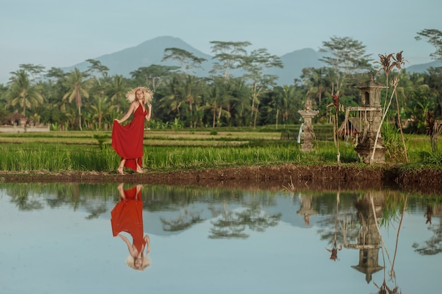 Una mujer con un vestido rojo y un sombrero camina en los campos de arroz en Bali.