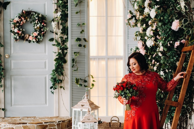 Una mujer con un vestido rojo se para y sostiene un ramo de rosas rojas y fresas en el interior.