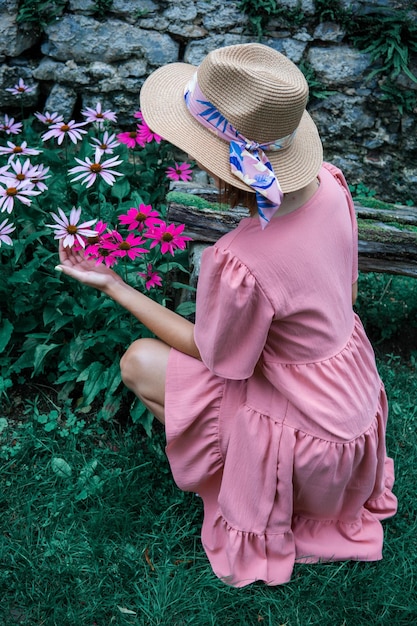 Foto mujer con vestido rosa en cuclillas para recoger flores en el jardín