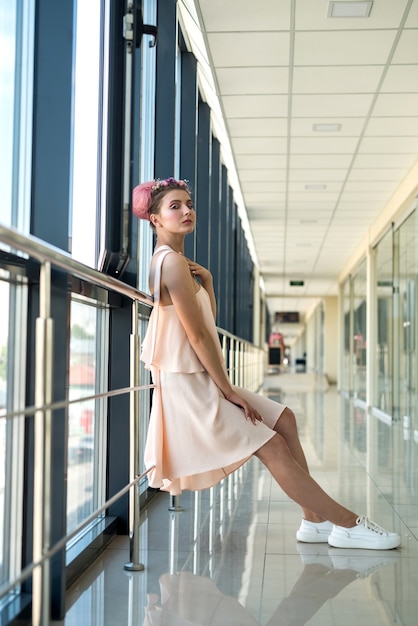 Mujer en vestido rosa de moda y zapatos blancos posando en el pasillo