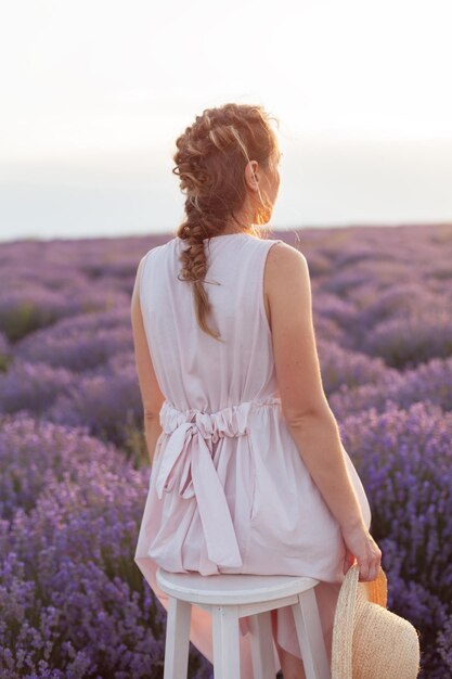 Mujer con vestido rosa y sombrero de mimbre fedora en el interminable campo de lavanda al atardecer. paisaje italiano