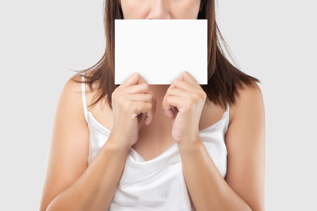 Una mujer en vestido de satén blanco sosteniendo un papel en blanco blanco contra un gris claro