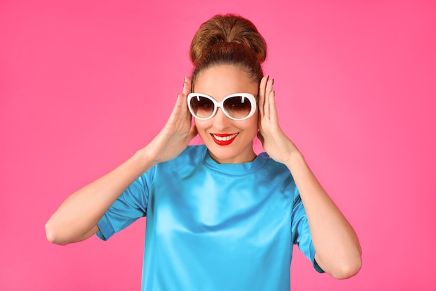 mujer con vestido de seda azul y gafas de sol blancas de fondo rosa