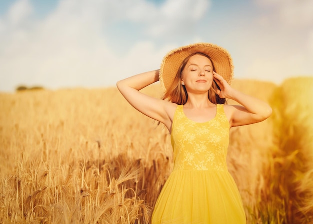 Mujer con vestido y sombrero caminando en un campo de trigo en verano