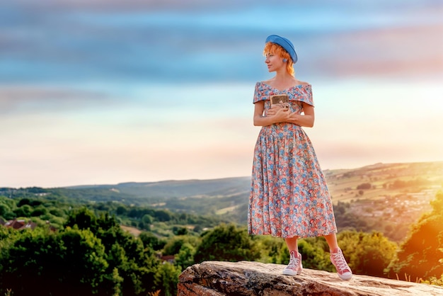 Mujer con vestido y sombrero con un ramo de lavanda en las manos en una colina al atardecer de verano