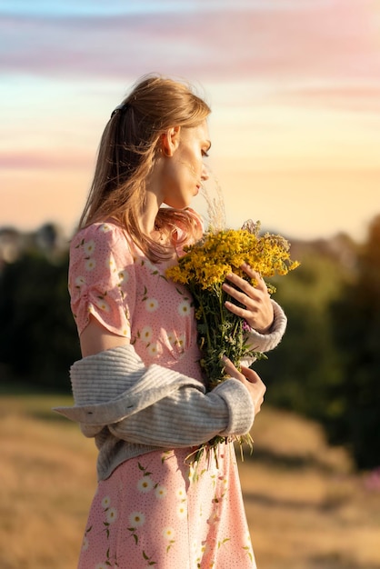 Mujer con vestido y sombrero con un ramo de lavanda en las manos en una colina al atardecer de verano