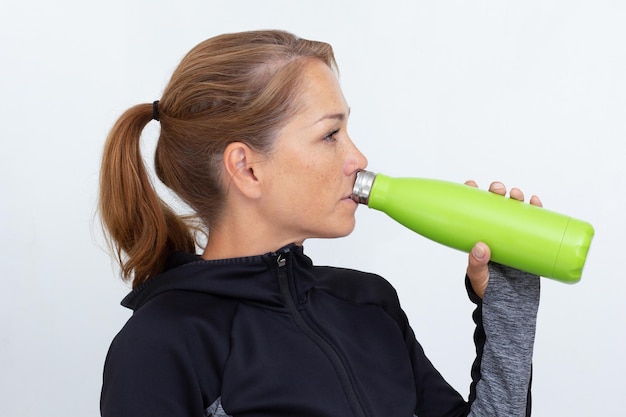 Mujer en vestido sportiv sosteniendo botella de termo verde bebiendo