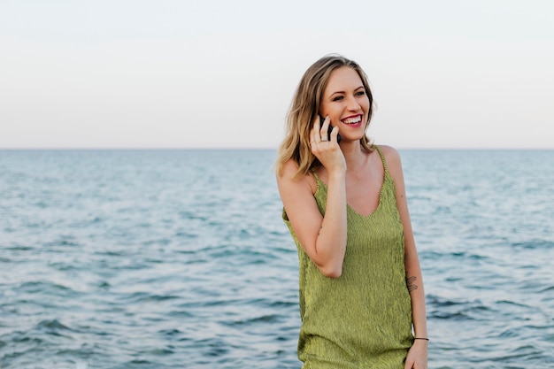 Mujer con un vestido verde hablando por su teléfono en la playa.