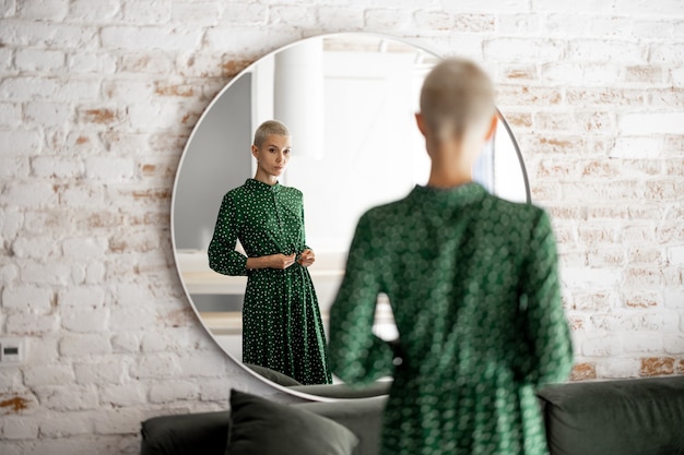 Foto mujer en vestido verde se mira en el espejo en casa