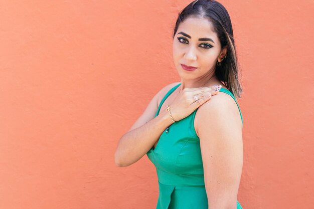 Mujer en vestido verde de pie delante de una pared roja.