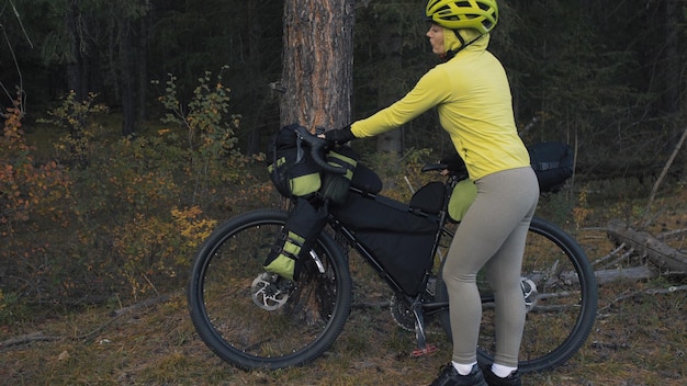 La mujer viaja en cicloturismo de terreno mixto con bicicleta bikepacking. El viajero viaja con bolsas para bicicletas. Parque forestal mágico.