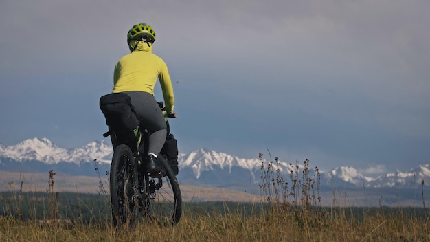 La mujer viaja en cicloturismo de terreno mixto con bikepacking El viaje del viajero con bolsas para bicicletas Deporte turismo bikepacking bicicleta ropa deportiva en colores verdes negros Montaña cubierta de nieve