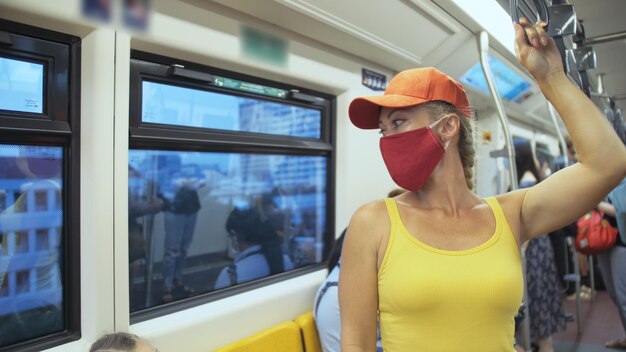 Mujer viaja en un paseo caucásico en un tren aéreo con una máscara roja médica protectora Chica turista en un tren aéreo con respirador Virus pandémico Coronavirus covid19 Personas con máscara