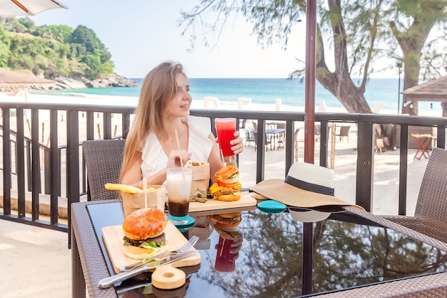 Mujer de viaje con bebidas de café y jugo de hamburguesas de comida rápida en la cafetería al aire libre