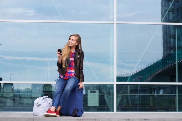 Mujer de viaje joven sentado en maleta mirando teléfono móvil