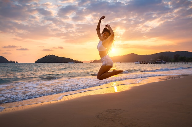 Mujer de viaje saltando en la playa en la puesta del sol