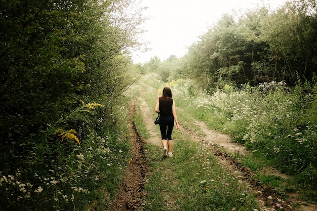 Foto mujer viajera elegante caminando a la luz del sol en el bosque con cámara fotográfica