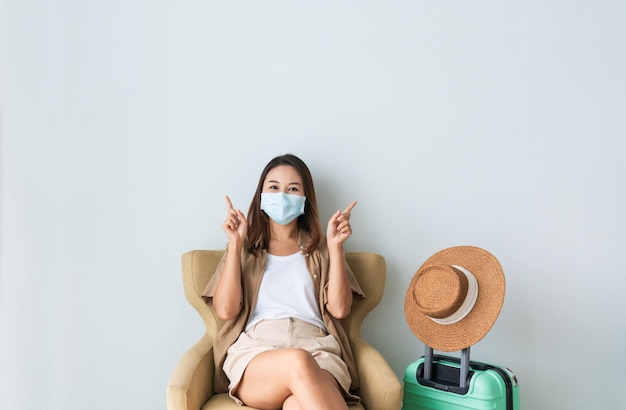 Mujer viajera feliz con mascarilla protectora apuntando con el dedo índice hacia arriba