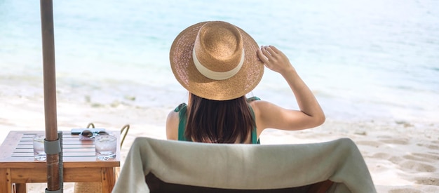 Mujer viajera feliz en traje de baño verde y sombrero disfrutar de hermosas vistas al mar mujer joven sentada en una silla en la playa de arena Libertad vacaciones relajantes vacaciones y concepto de viaje de verano