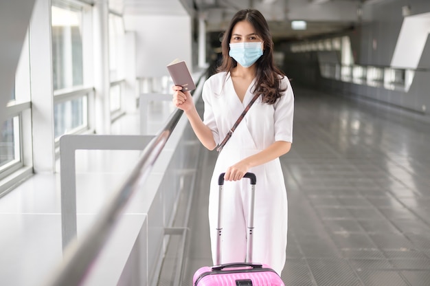 Una mujer viajera lleva una máscara protectora en el aeropuerto internacional, viaja bajo la pandemia de Covid-19, viajes de seguridad, protocolo de distanciamiento social, nuevo concepto de viaje normal.