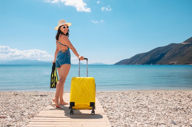 Mujer viajera con maleta y aletas en la playa caminando hacia el mar