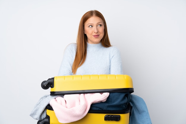 Mujer viajera con una maleta llena de ropa de pie y mirando a un lado