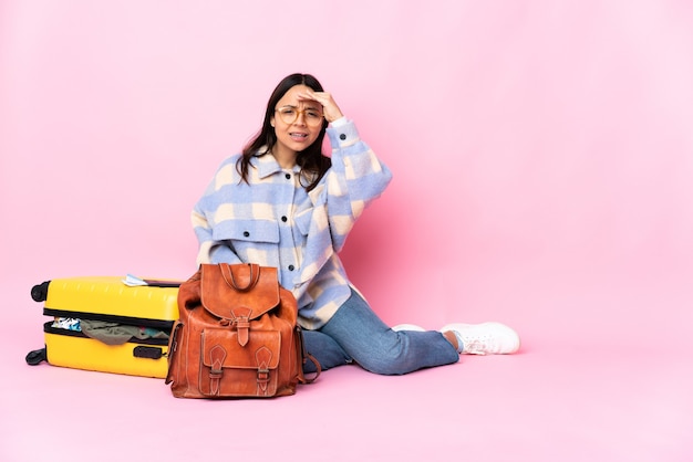 Mujer viajera con una maleta sentada en el suelo mirando lejos con la mano para buscar algo