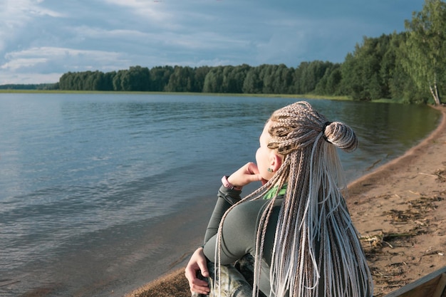 mujer viajera con peinado de trenzas sentada en una orilla de arena de un vasto lago