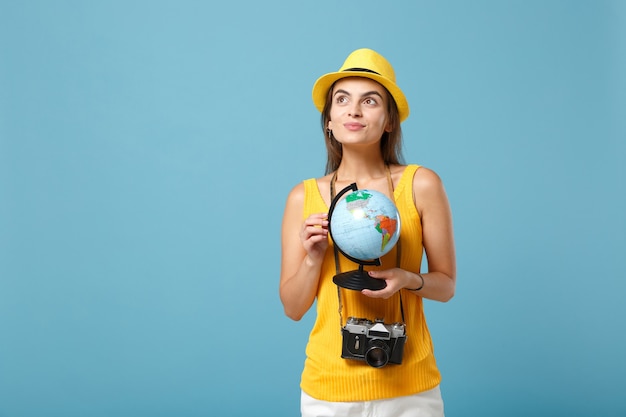 Mujer viajera en ropa casual de verano amarillo y sombrero con globo y cámara en azul