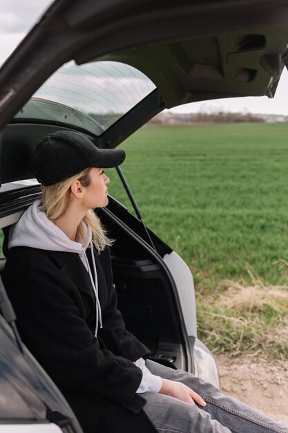 Mujer viajera sentada en un auto hatchback con fondo de montaña en tono vintage