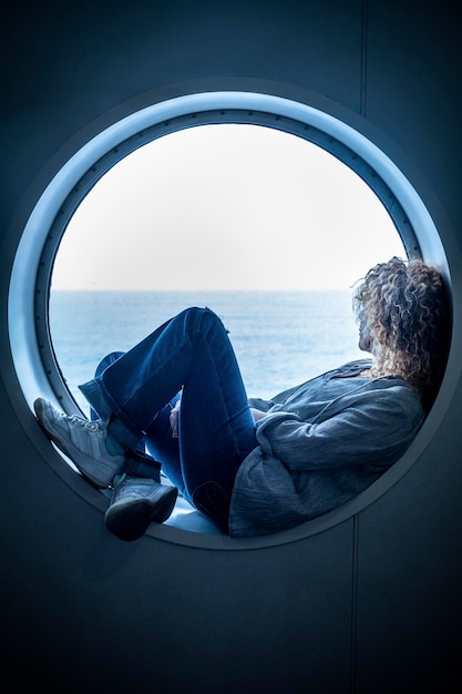 Mujer viajera sentada dentro de un ojo de buey en el crucero en barco disfrutando del viaje y la aventura del viaje solo contemplando el agua del océano Concepto de transporte por mar y mujeres