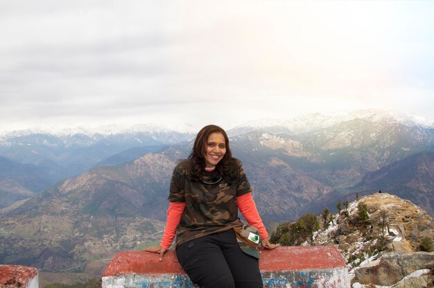 Foto mujer viajera sentada fuera del templo de kartik swami y mirando a la cámara y la cordillera