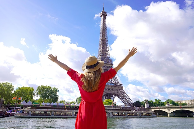 Mujer viajera con sombrero y brazos levantados en el río Sena en París Vista posterior de la mujer de moda con los brazos abiertos en París hermosa vista con la Torre Eiffel al fondo