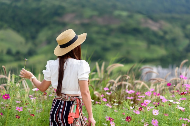 Mujer viajera sosteniendo una flor con sombrero y mirando montañas verdes y espacio de concepto de viaje de vacaciones en el bosque para texto