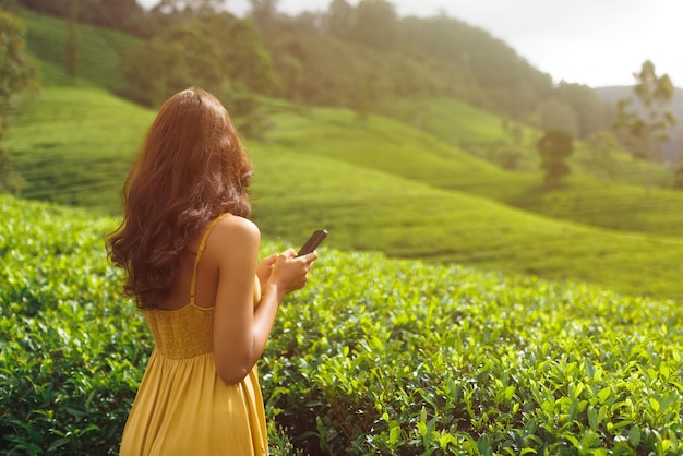 Mujer viajera con teléfono inteligente durante su viaje en famosas plantaciones de té de la naturaleza en sri la