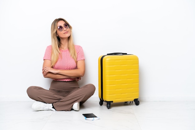 Foto mujer viajera uruguaya sentada en el suelo aislada de fondo blanco mirando hacia arriba mientras sonríe