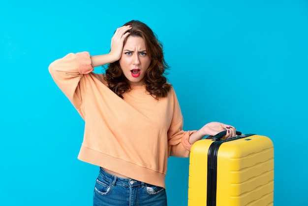 Mujer del viajero con maleta sobre fondo azul aislado con expresión facial sorpresa