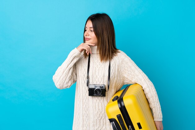 Foto mujer del viajero que sostiene una maleta amarilla sobre la pared azul aislada
