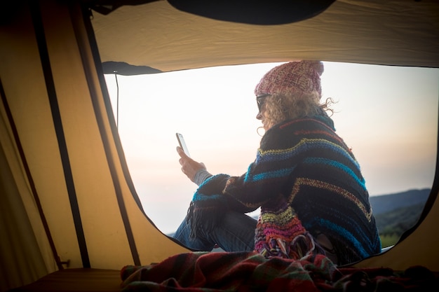 Foto la mujer de viajes moderna usa la conexión a internet y el teléfono móvil fuera de la carpa en la naturaleza - concepto de viaje y comunicación - gente libre y vacaciones alternativas