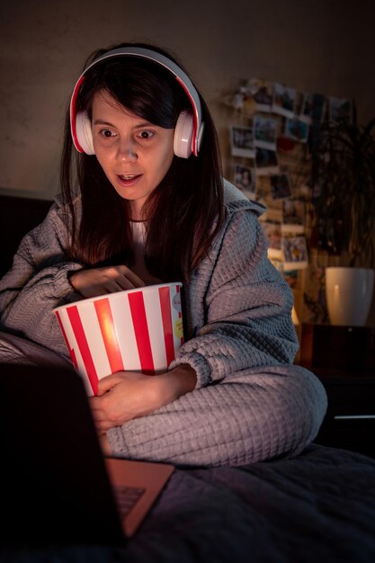 Foto mujer viendo una película de miedo en casa comiendo auriculares de palomitas de maíz