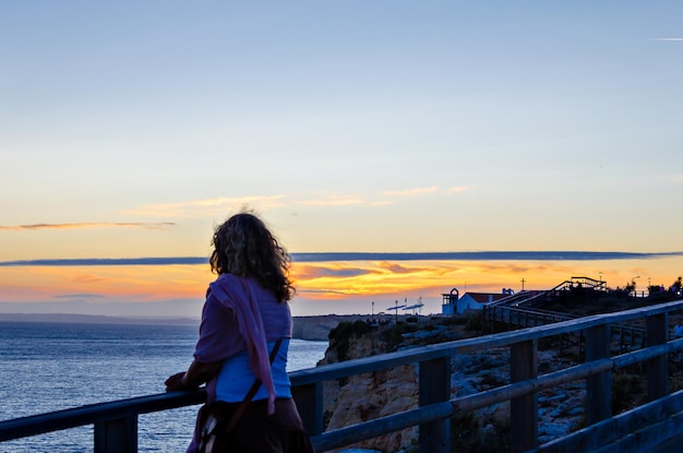 Mujer viendo la puesta de sol en la playa de Carvoeiro en Lagoa, región de Algarve, Portugal. Romántico.