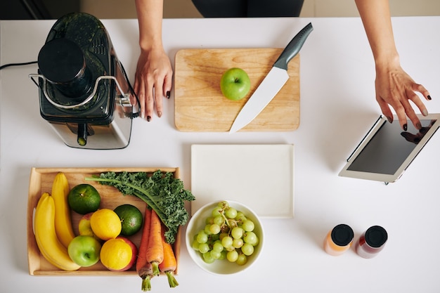 Foto mujer viendo el video de un blogger de alimentos en una tableta al hacer un batido sabroso y saludable con col rizada, frutas y verduras, vista desde la parte superior