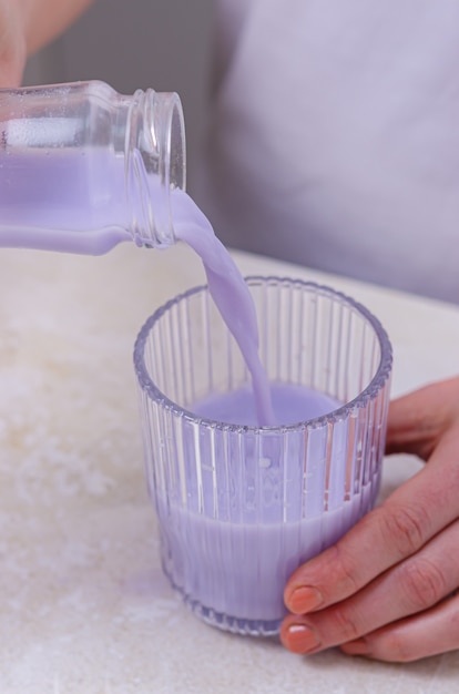 Mujer vierte leche de lavanda en un vaso de una botella. Bebe una bebida con una pajita. Cuidado de la salud